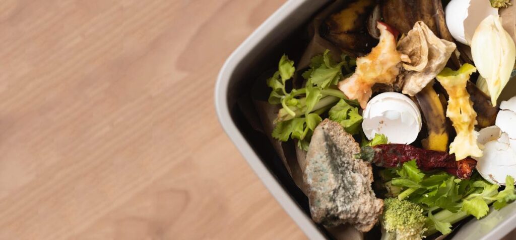 Cubo reciclaje con restos de alimentos con fondo suelo de madera.